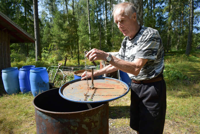 Klaus Peurla polttaa biohiiltä peltitynnyrissä. Vesijohto on lähellä, jotta mahdolliset sinkoilevat kipinät saa sammutettua heti.